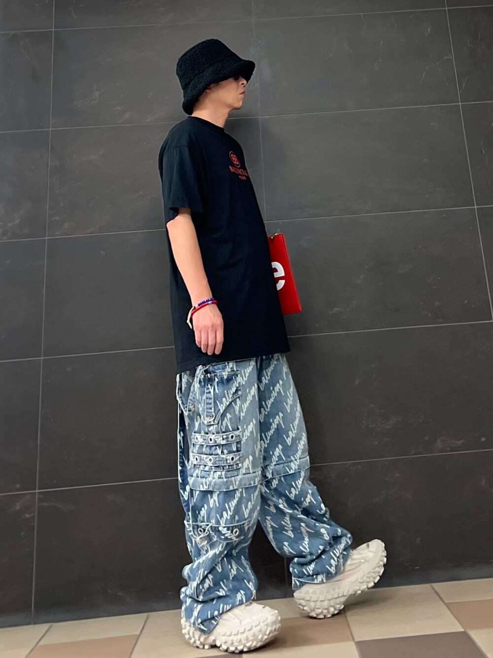 レッド系のクラッチバッグ、ブルー系のデニムパンツ、ベージュ系のスニーカーを着用したメンズの夏コーディネートの3枚目の写真