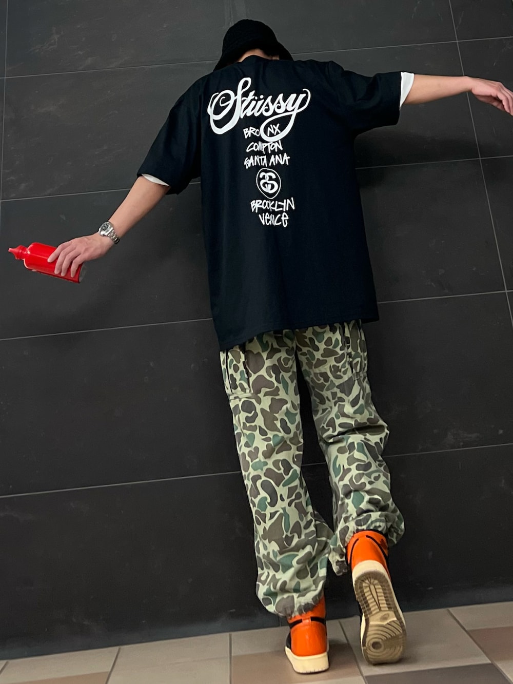 グリーン系のカーゴパンツ、オレンジ系のスニーカー、ブラック系のTシャツ/カットソーを着用したメンズの夏コーディネートの2枚目の写真