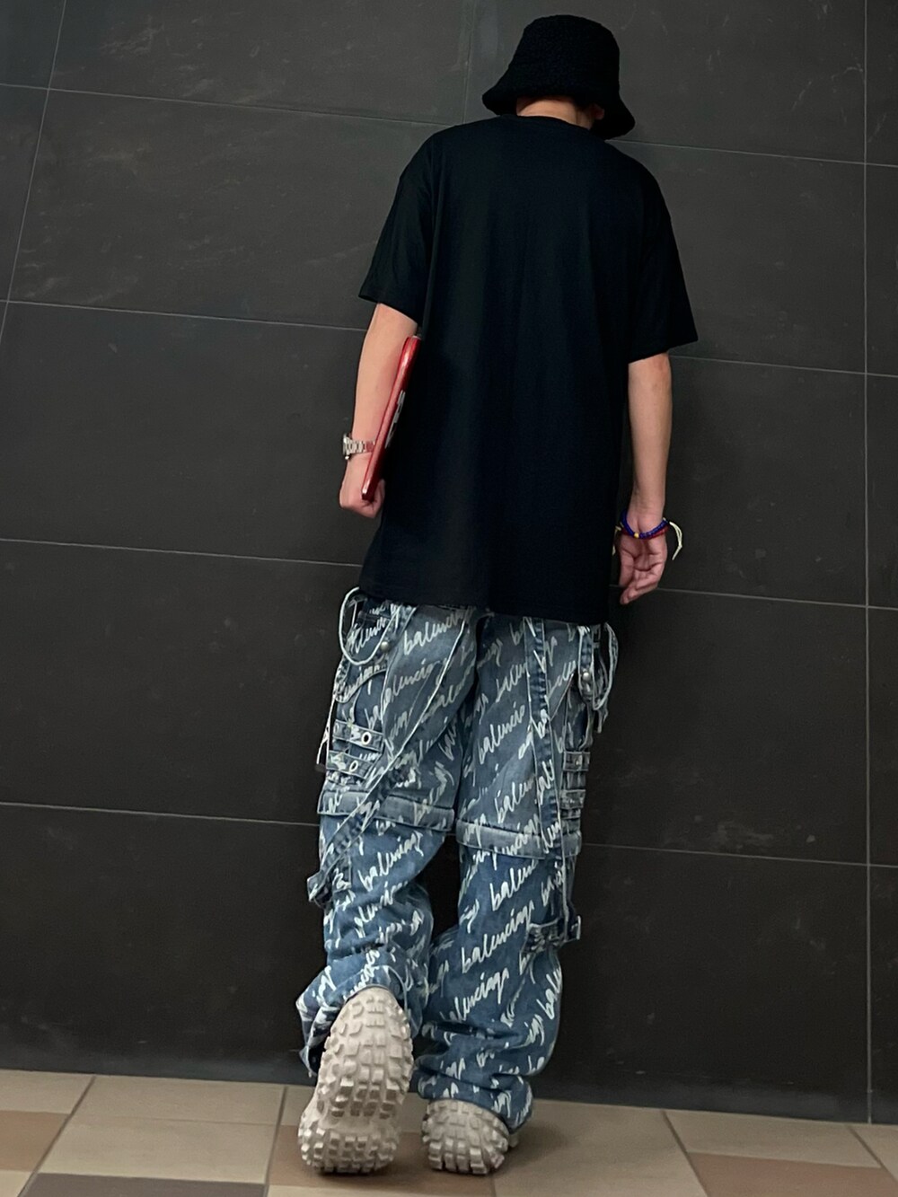 レッド系のクラッチバッグ、ブルー系のデニムパンツ、ベージュ系のスニーカーを着用したメンズの夏コーディネートの4枚目の写真