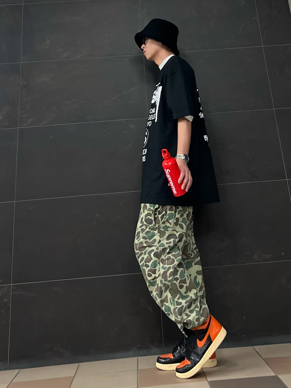 グリーン系のカーゴパンツ、オレンジ系のスニーカー、ブラック系のTシャツ/カットソーを着用したメンズの夏コーディネートの3枚目の写真