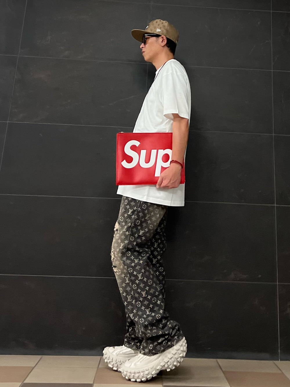 ホワイト系のTシャツ/カットソー、レッド系のクラッチバッグ、ブラック系のデニムパンツを着用したメンズの夏コーディネートの2枚目の写真