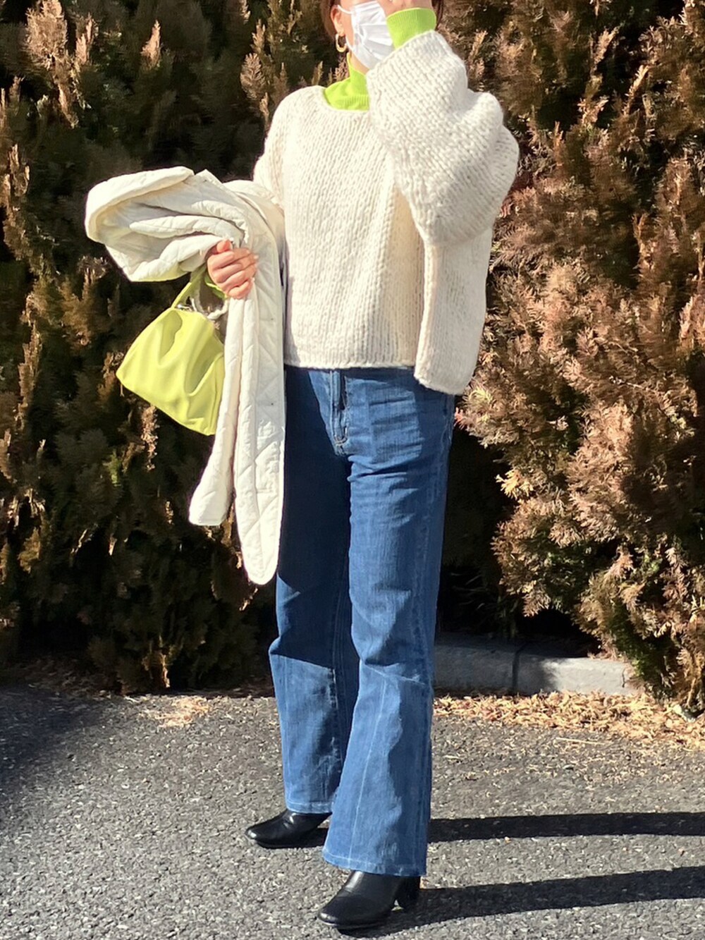 イエロー系のショルダーバッグ、ホワイト系のニット/セーター、ブルー系のデニムパンツを着用したレディースの冬コーディネートの2枚目の写真