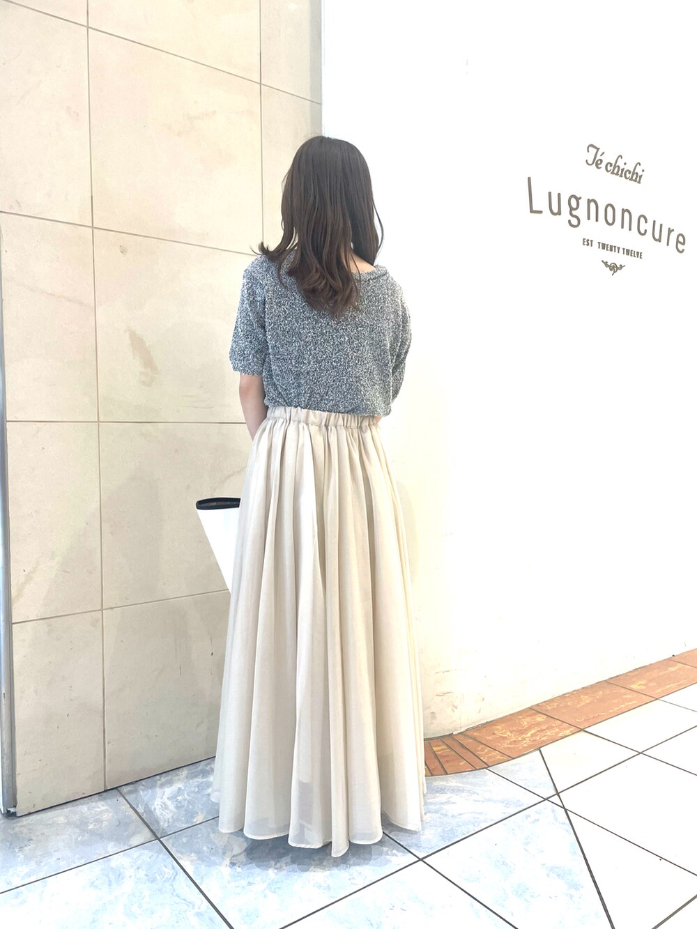 グレー系のカーディガン/ボレロ、ホワイト系のスカート、ホワイト系のハンドバッグを着用したレディースの春コーディネートの2枚目の写真