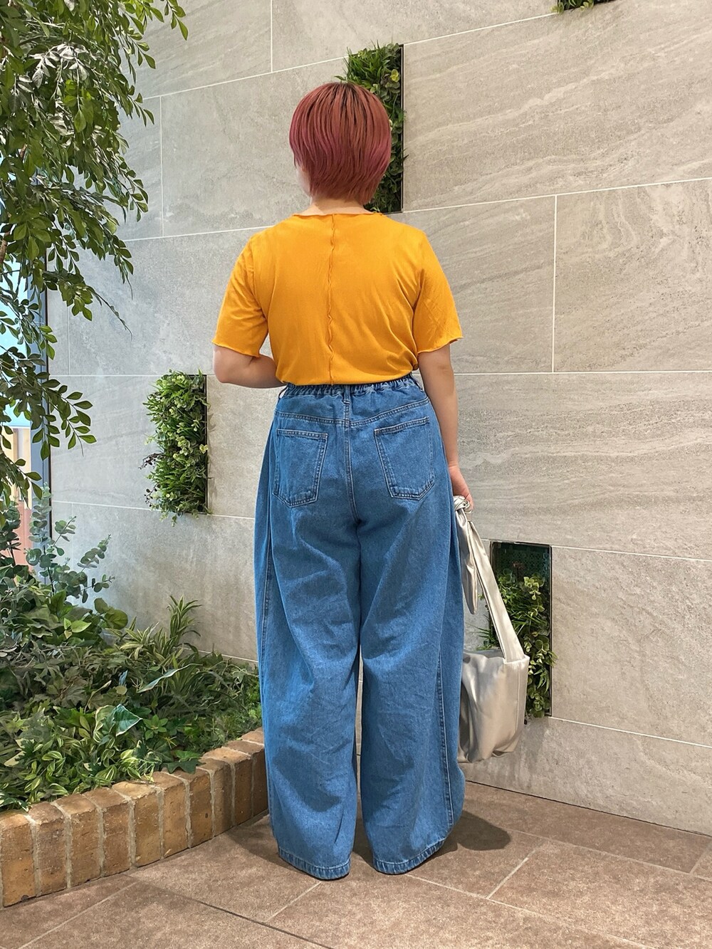 オレンジ系のTシャツ/カットソー、シルバー系のハンドバッグ、ブルー系のデニムパンツを着用したレディースの春コーディネートの2枚目の写真