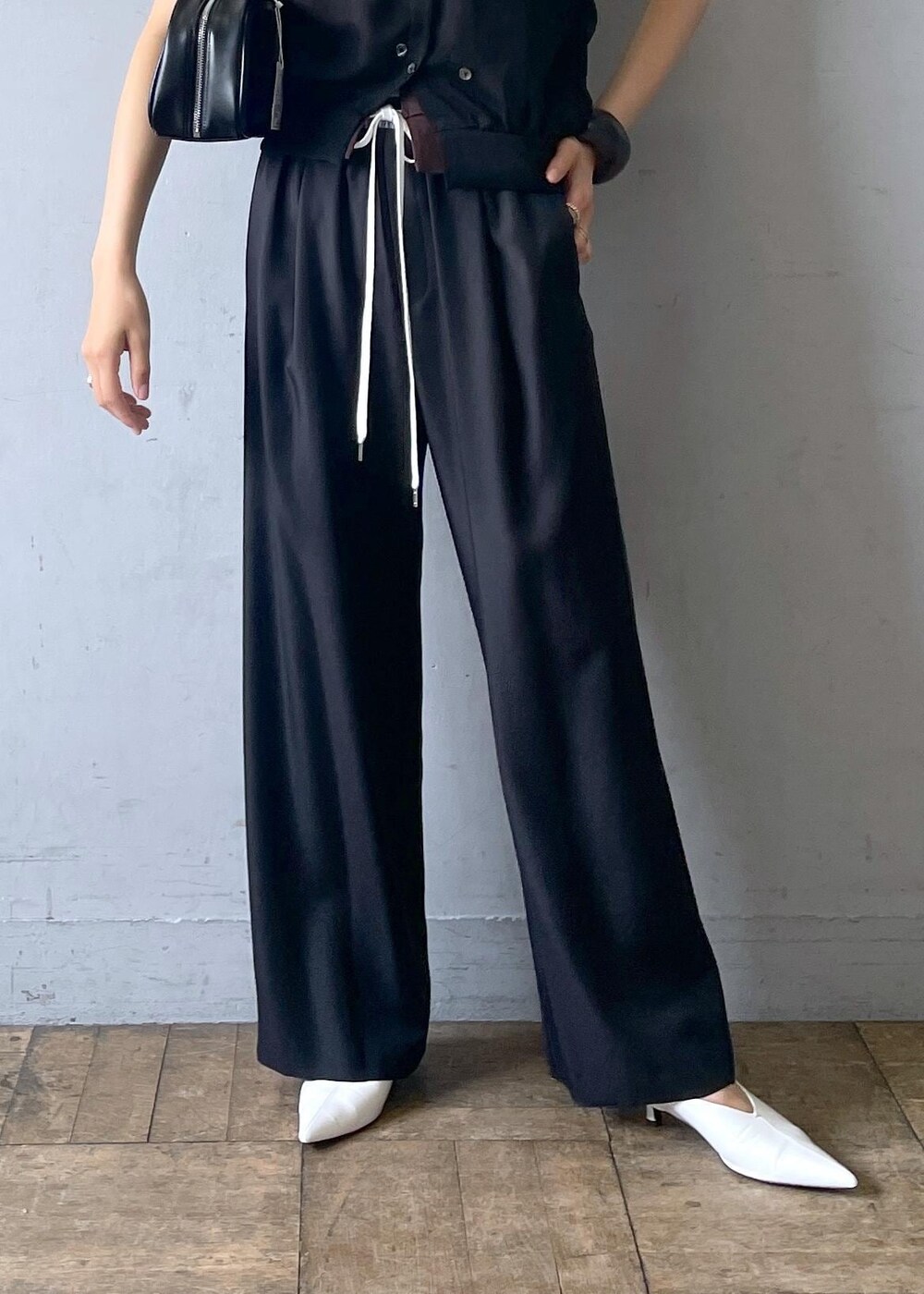 ブラック系のボストンバッグ、ホワイト系のパンプス、ブラック系のスラックスを着用したレディースの夏コーディネートの7枚目の写真