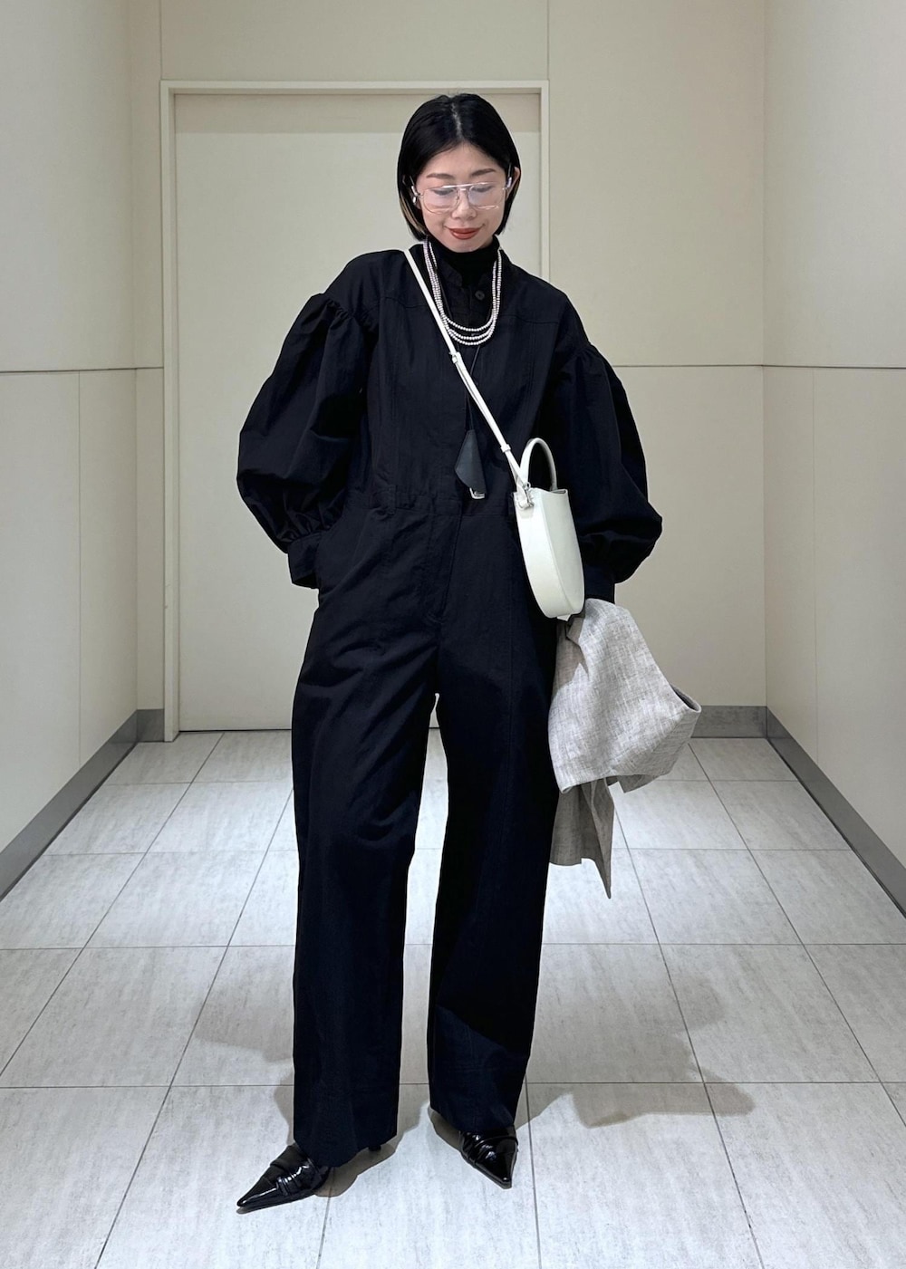 ホワイト系のハンドバッグ、ベージュ系のベスト、ブラック系のつなぎ/オールインワンを着用したレディースの冬コーディネートの3枚目の写真