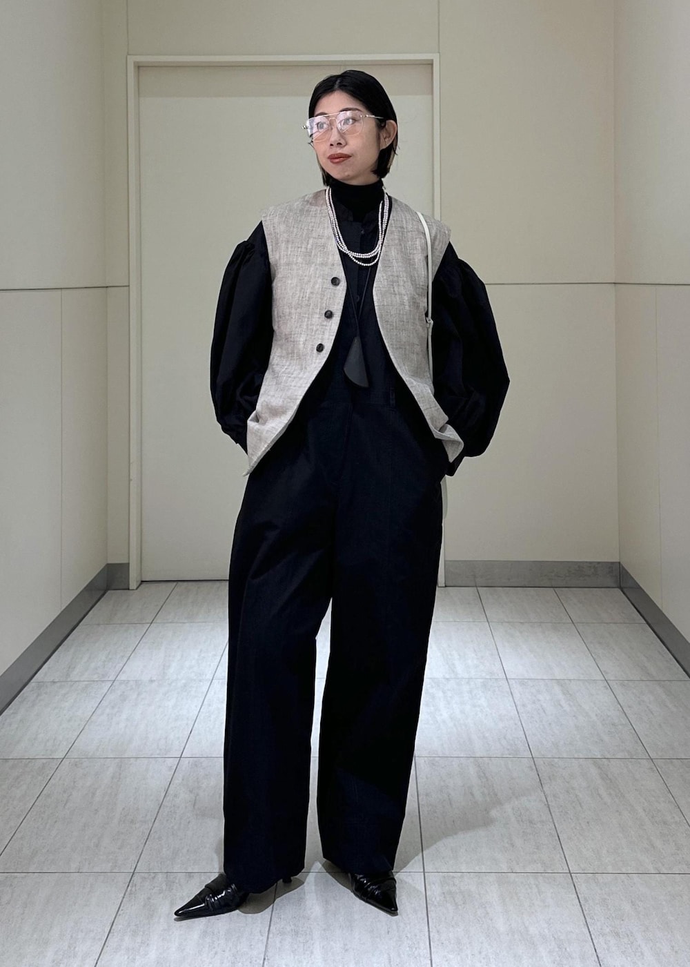 ホワイト系のハンドバッグ、ベージュ系のベスト、ブラック系のつなぎ/オールインワンを着用したレディースの冬コーディネートの2枚目の写真