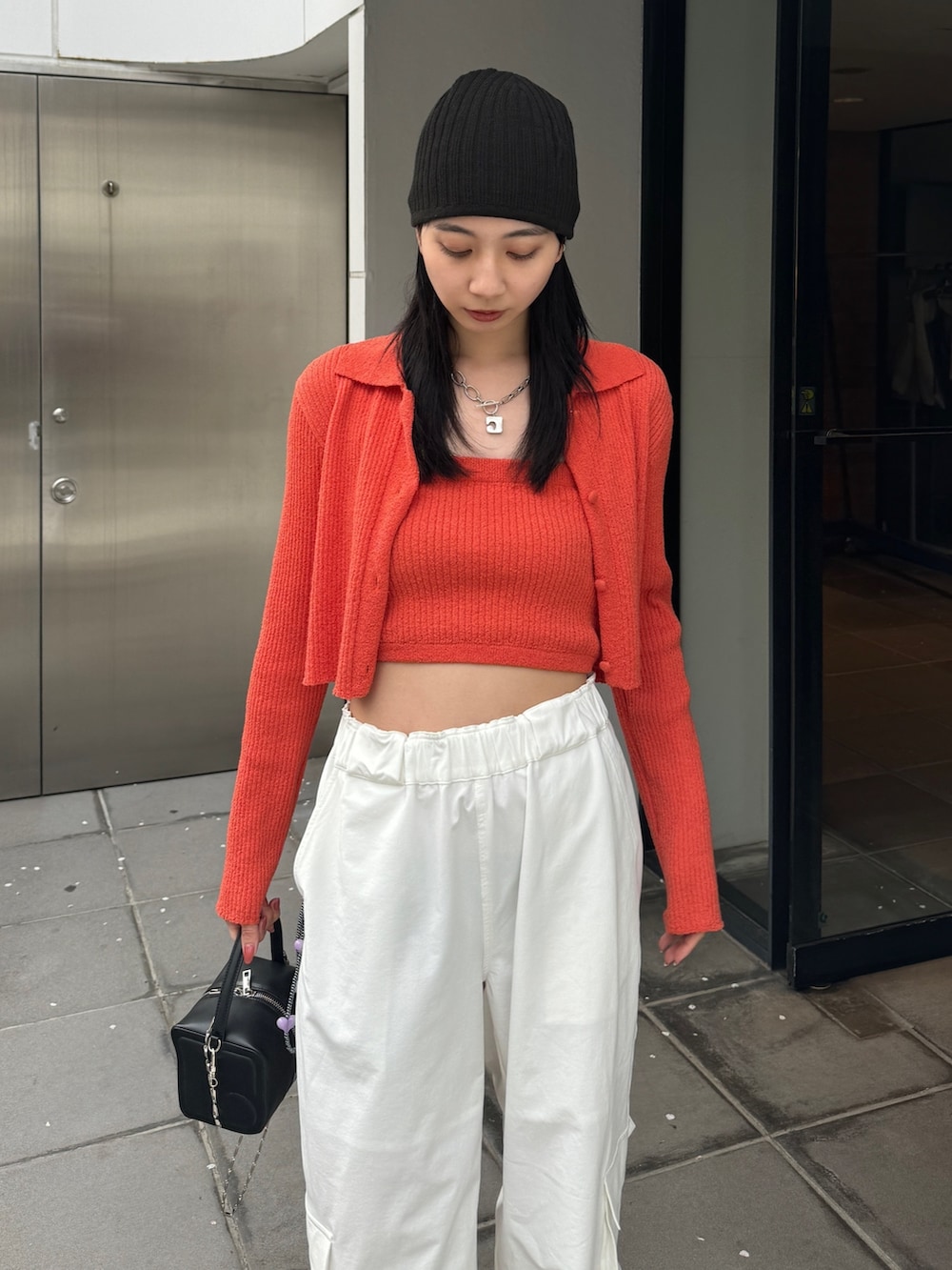 オレンジ系のニット/セーター、ホワイト系のカーゴパンツを着用したレディースの春コーディネートの2枚目の写真