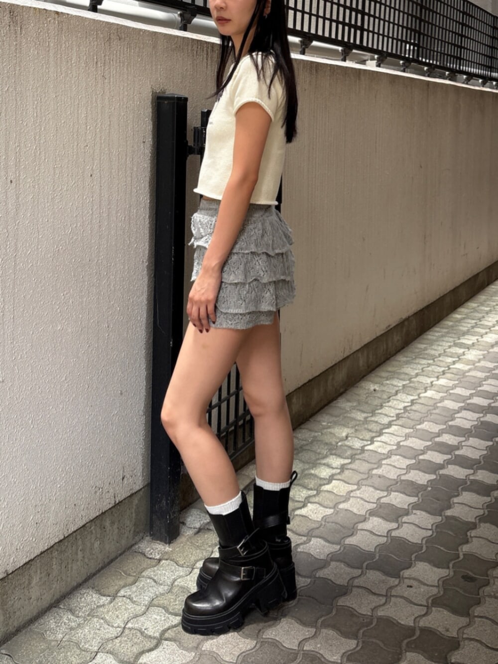 ブラック系のブーツ、ホワイト系のニット/セーター、グレー系のスカートを着用したレディースの夏コーディネートの2枚目の写真
