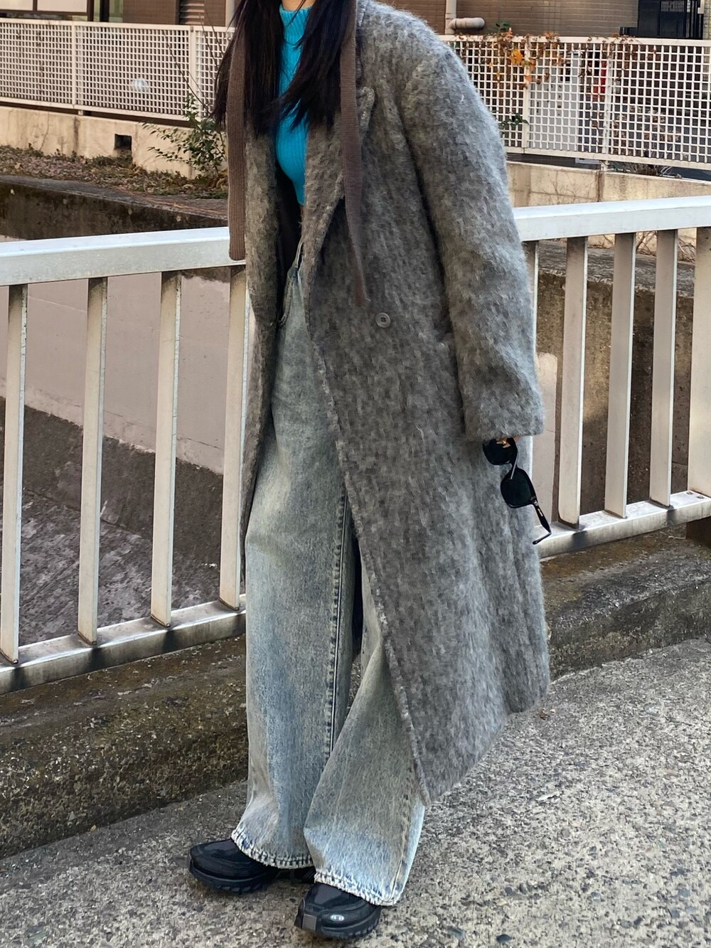 グレー系のチェスターコート、ブルー系のデニムパンツ、ブルー系のニット/セーターを着用したレディースの冬コーディネートの2枚目の写真