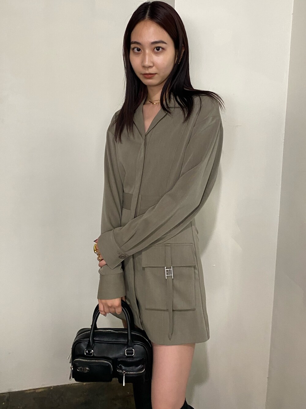 ブラック系のハンドバッグ、ベージュ系のワンピース、ブラック系のブーツを着用したレディースの秋コーディネートの2枚目の写真