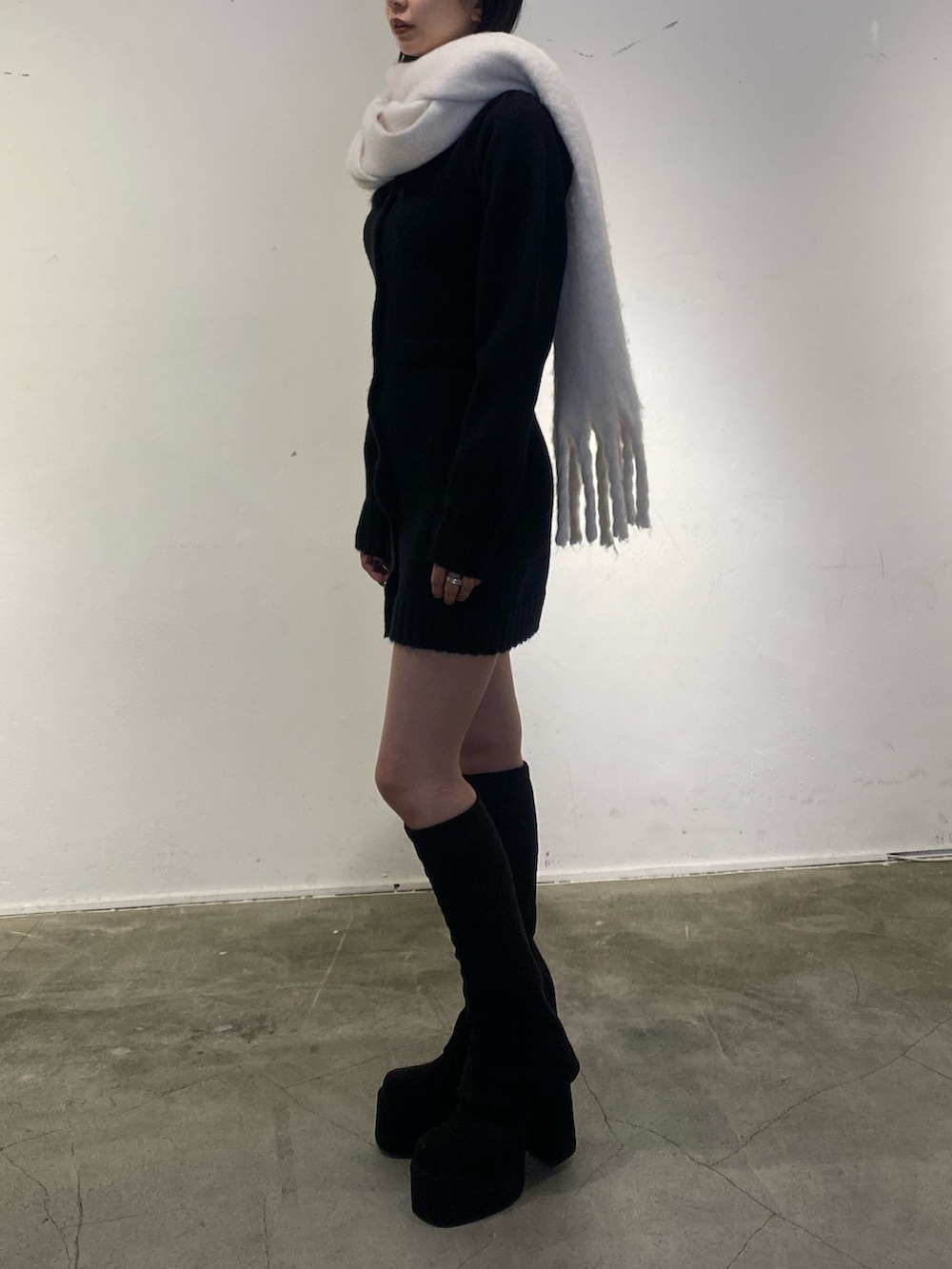 ブラック系のワンピース、ブラック系のブーツ、ホワイト系のマフラーを着用したレディースの秋コーディネートの2枚目の写真