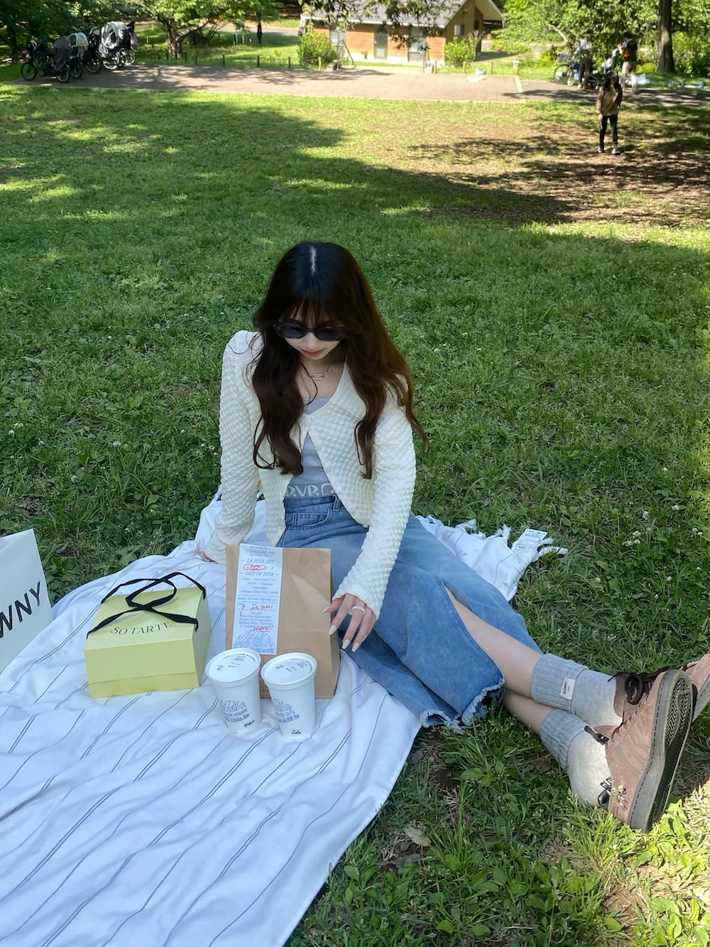 ホワイト系のカーディガン/ボレロ、ベージュ系のショルダーバッグ、ブルー系のデニムスカートを着用したレディースの夏コーディネートの2枚目の写真