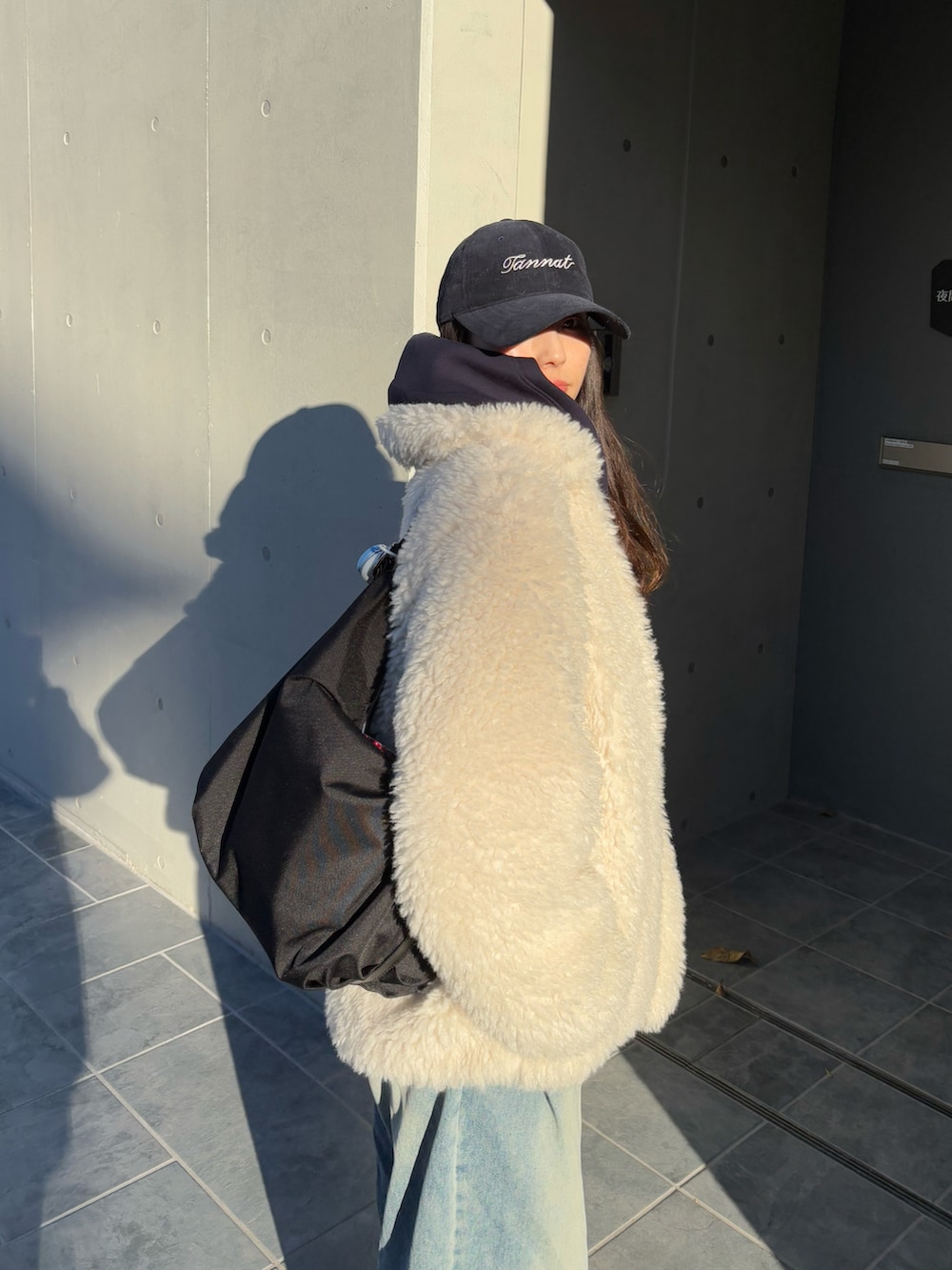 ホワイト系のステンカラーコート、ブルー系のデニムパンツ、ブラック系のスニーカーを着用したレディースの冬コーディネートの2枚目の写真