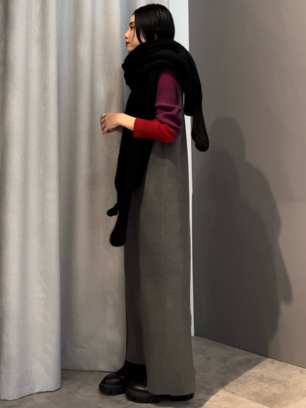 グレー系のワンピース、ブラック系のブーツ、ブラック系のマフラーを着用したレディースの秋コーディネートの2枚目の写真