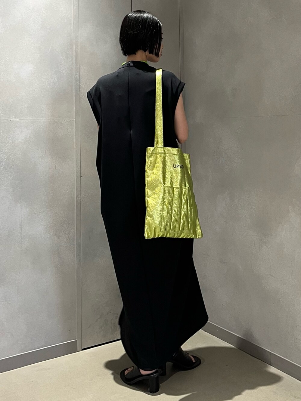 ブラック系のワンピース、ブラック系のサンダル、イエロー系のトートバッグを着用したレディースの夏コーディネートの3枚目の写真