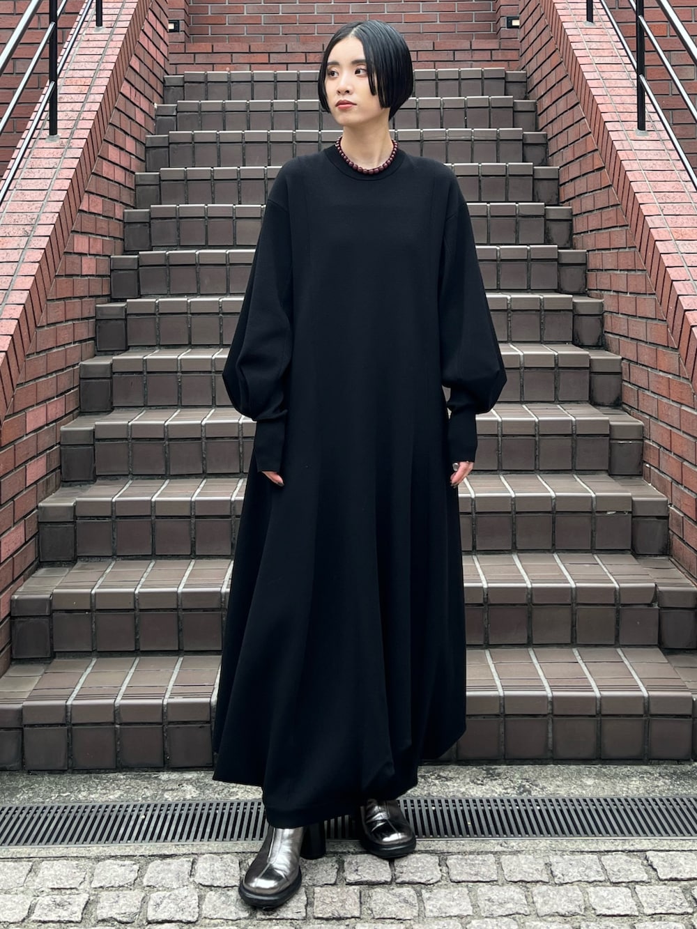 ブラック系のワンピース、シルバー系のブーツ、ブラウン系のネックレスを着用したレディースの秋コーディネートの2枚目の写真