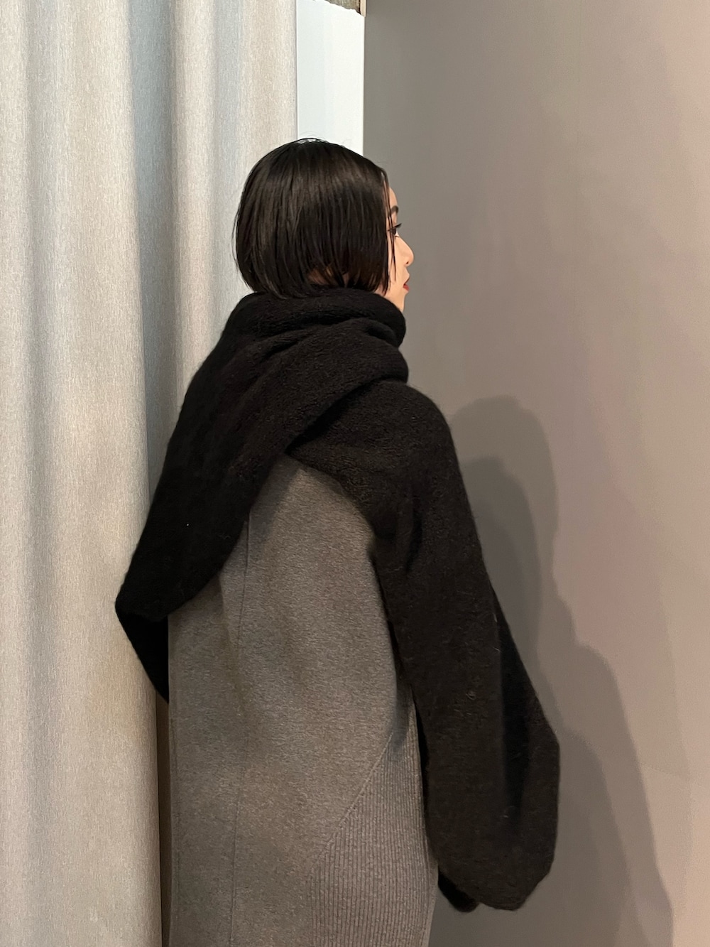 グレー系のワンピース、ブラック系のブーツ、ブラック系のマフラーを着用したレディースの秋コーディネートの4枚目の写真