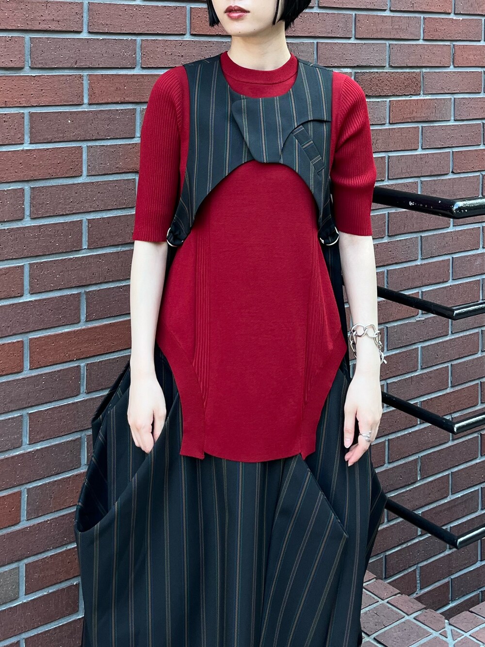 レッド系のニット/セーター、ブラック系のベスト、ブラック系のスカートを着用したレディースの夏コーディネートの6枚目の写真