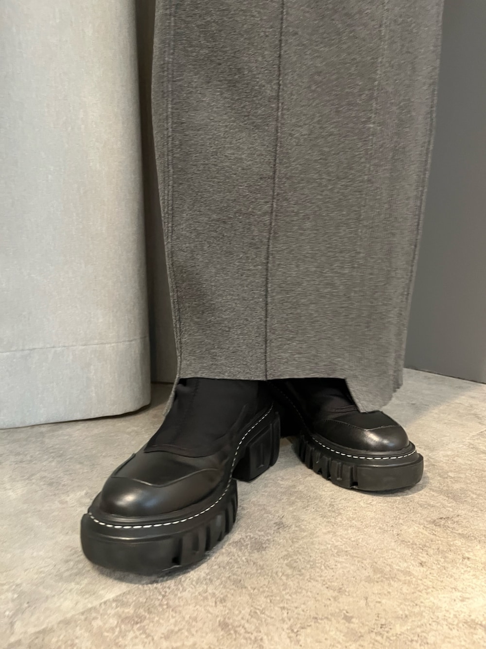 グレー系のワンピース、ブラック系のブーツ、ブラック系のマフラーを着用したレディースの秋コーディネートの9枚目の写真