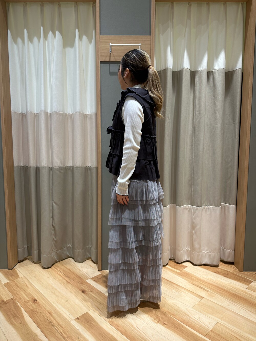 ブラック系のベスト、ホワイト系のTシャツ/カットソー、グレー系のスカートを着用したレディースの冬コーディネートの2枚目の写真