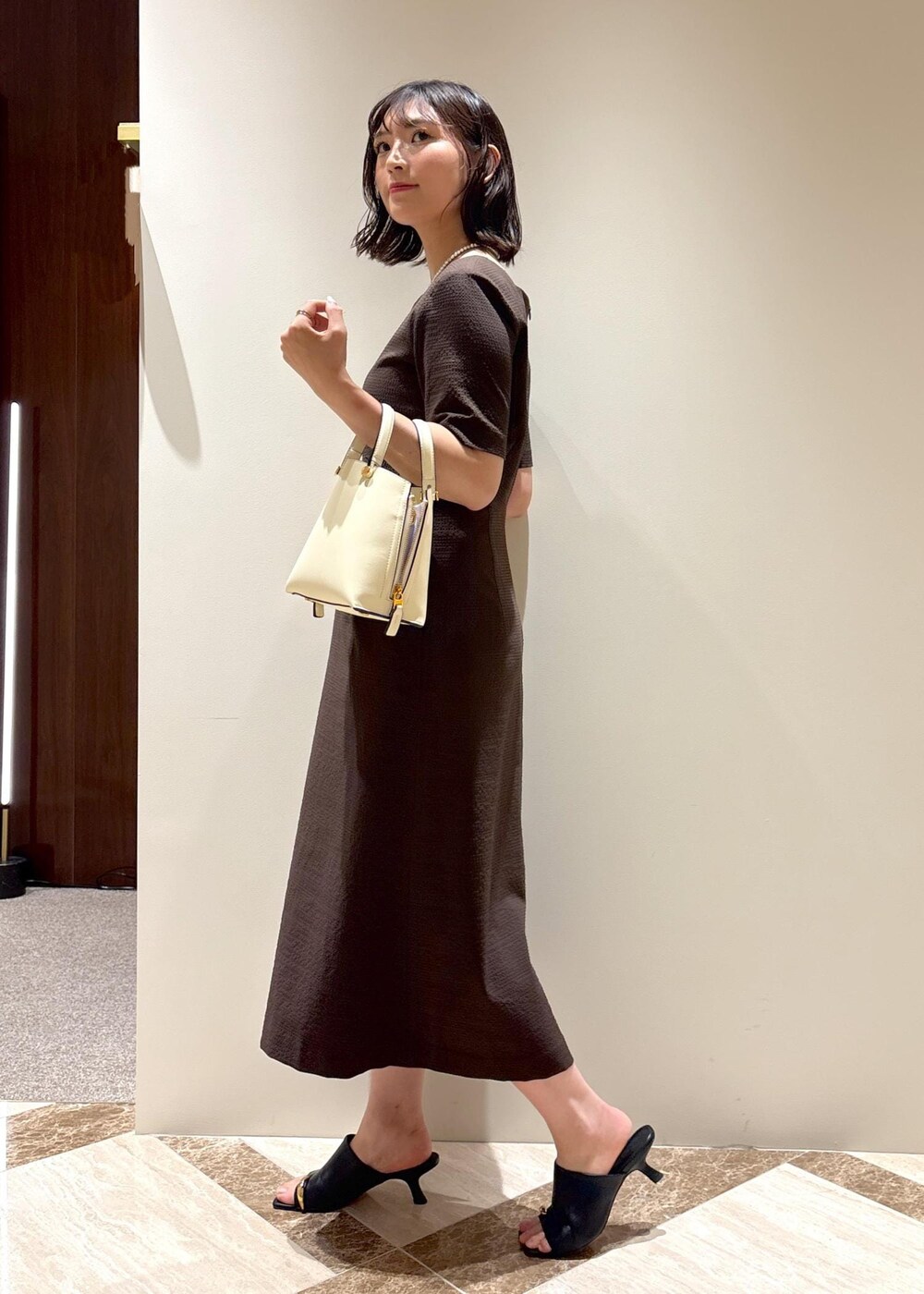ホワイト系のハンドバッグ、ブラック系のサンダル、ブラウン系のワンピースを着用したレディースの夏コーディネートの3枚目の写真