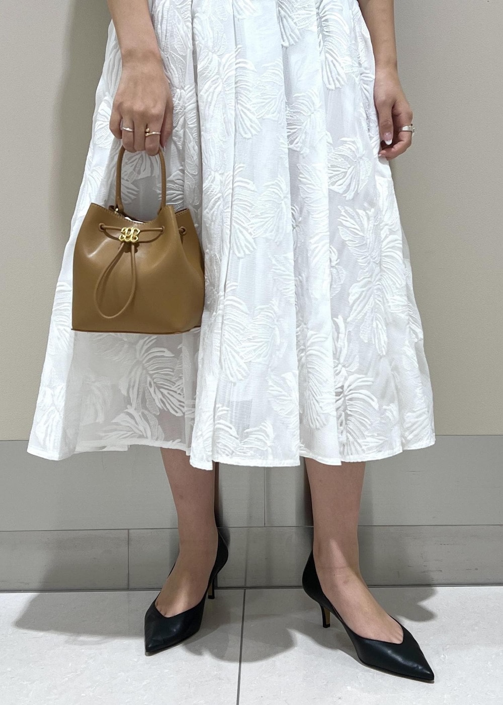 イエロー系のハンドバッグ、ホワイト系のスカート、ブラック系のニット/セーターを着用したレディースの冬コーディネートの6枚目の写真