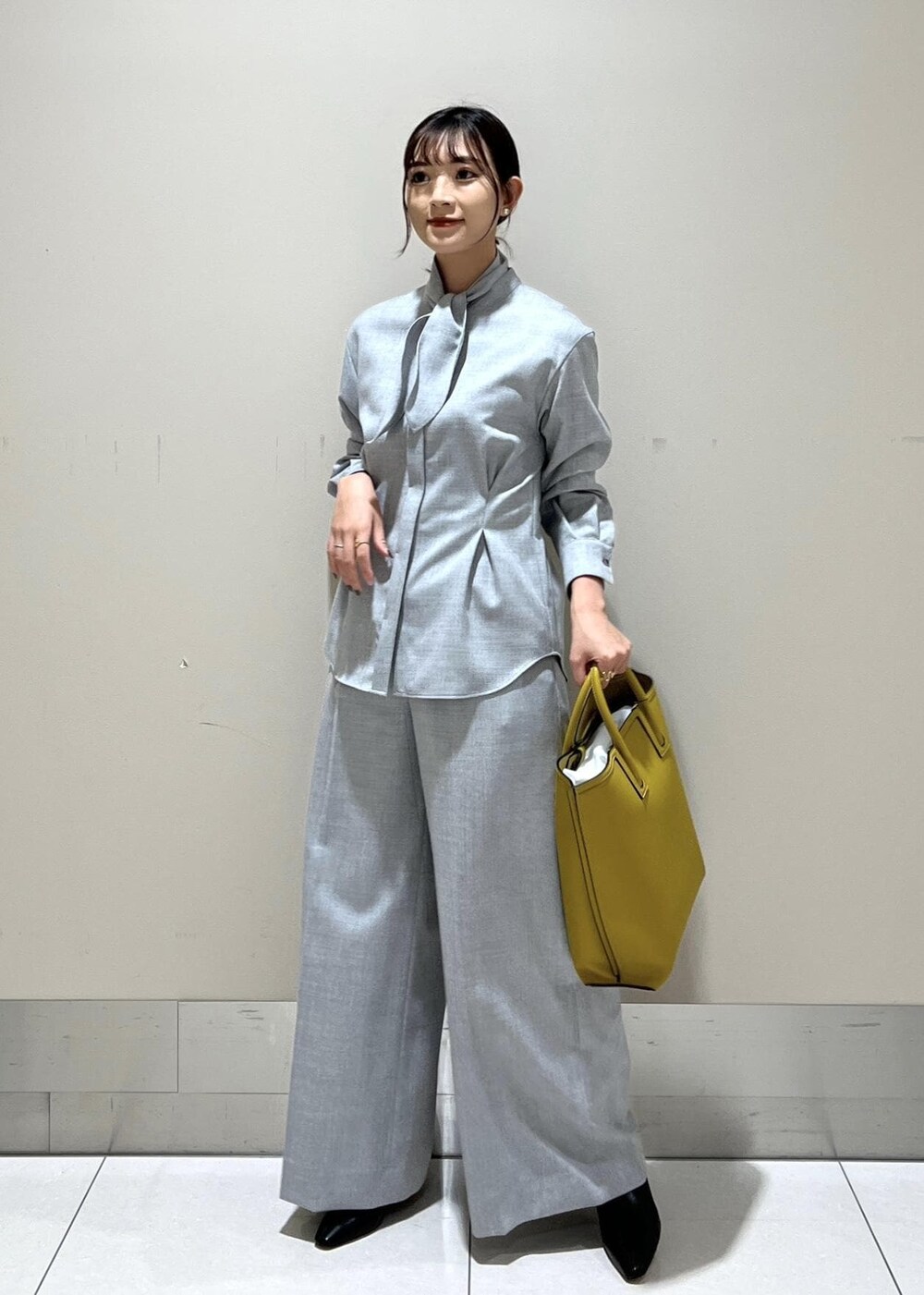 イエロー系のトートバッグ、ブラック系のブーツ、グレー系のシャツ/ブラウスを着用したレディースの秋コーディネートの2枚目の写真