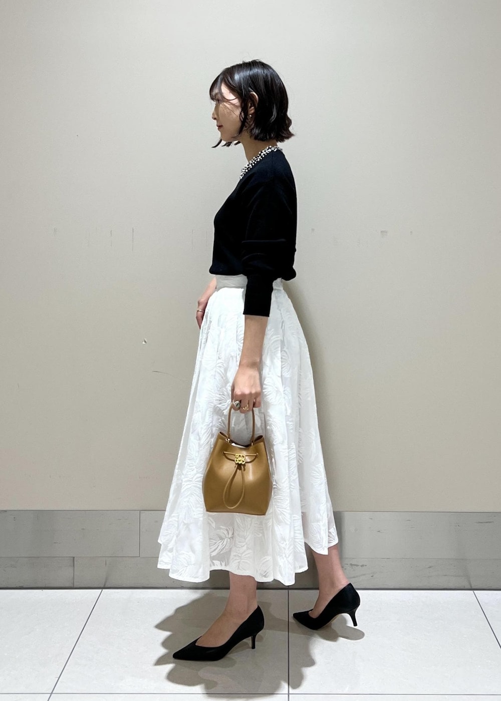 イエロー系のハンドバッグ、ホワイト系のスカート、ブラック系のニット/セーターを着用したレディースの冬コーディネートの2枚目の写真