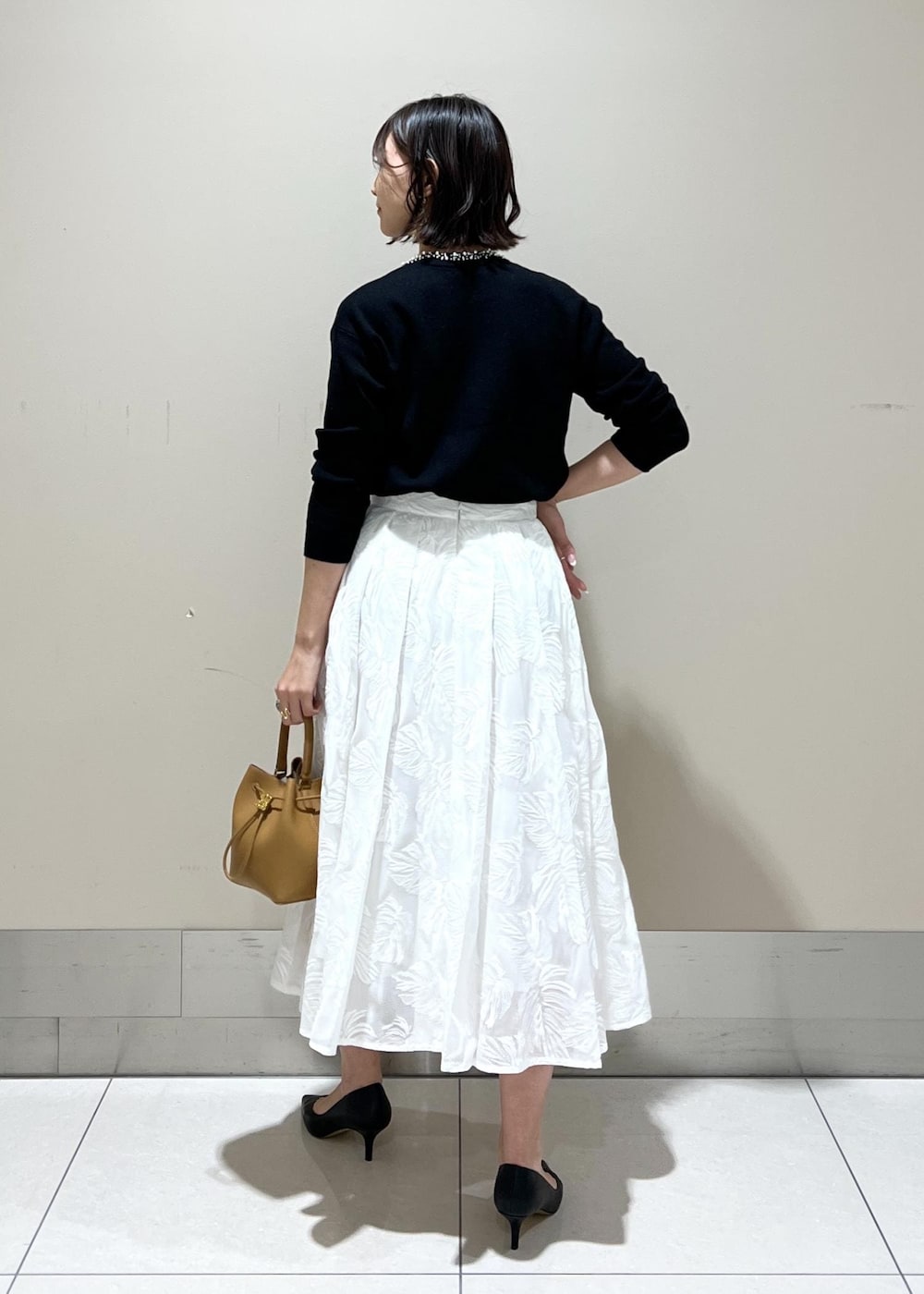 イエロー系のハンドバッグ、ホワイト系のスカート、ブラック系のニット/セーターを着用したレディースの冬コーディネートの3枚目の写真