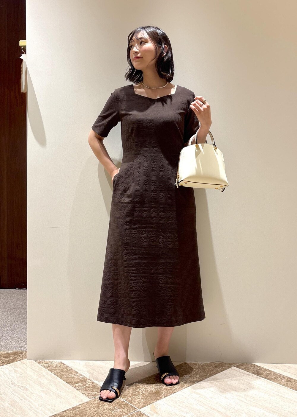 ホワイト系のハンドバッグ、ブラック系のサンダル、ブラウン系のワンピースを着用したレディースの夏コーディネートの2枚目の写真