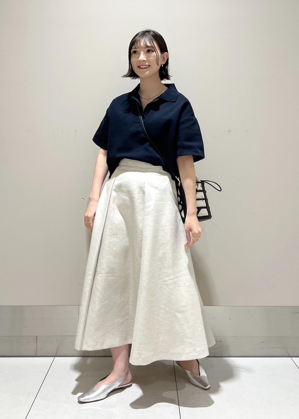 ブラック系のハンドバッグ、シルバー系のパンプス、ブルー系のニット/セーターを着用したレディースの春コーディネートの2枚目の写真