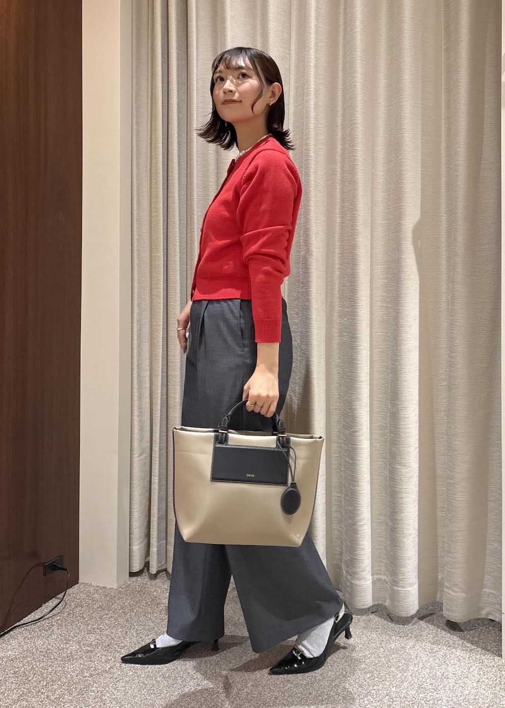 ベージュ系のトートバッグ、ブルー系のスラックス、レッド系のカーディガン/ボレロを着用したレディースの冬コーディネートの3枚目の写真