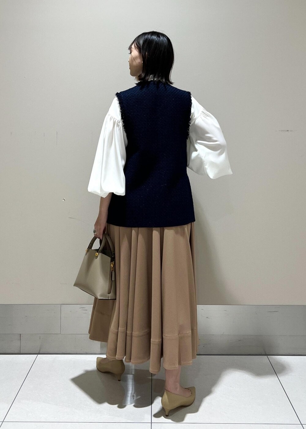 ベージュ系のパンプス、ベージュ系のハンドバッグ、イエロー系のスカートを着用したレディースの冬コーディネートの3枚目の写真