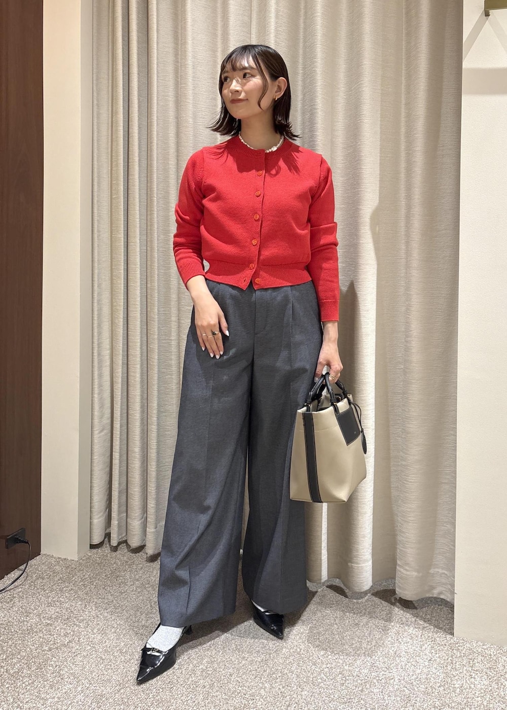 ベージュ系のトートバッグ、ブルー系のスラックス、レッド系のカーディガン/ボレロを着用したレディースの冬コーディネートの2枚目の写真