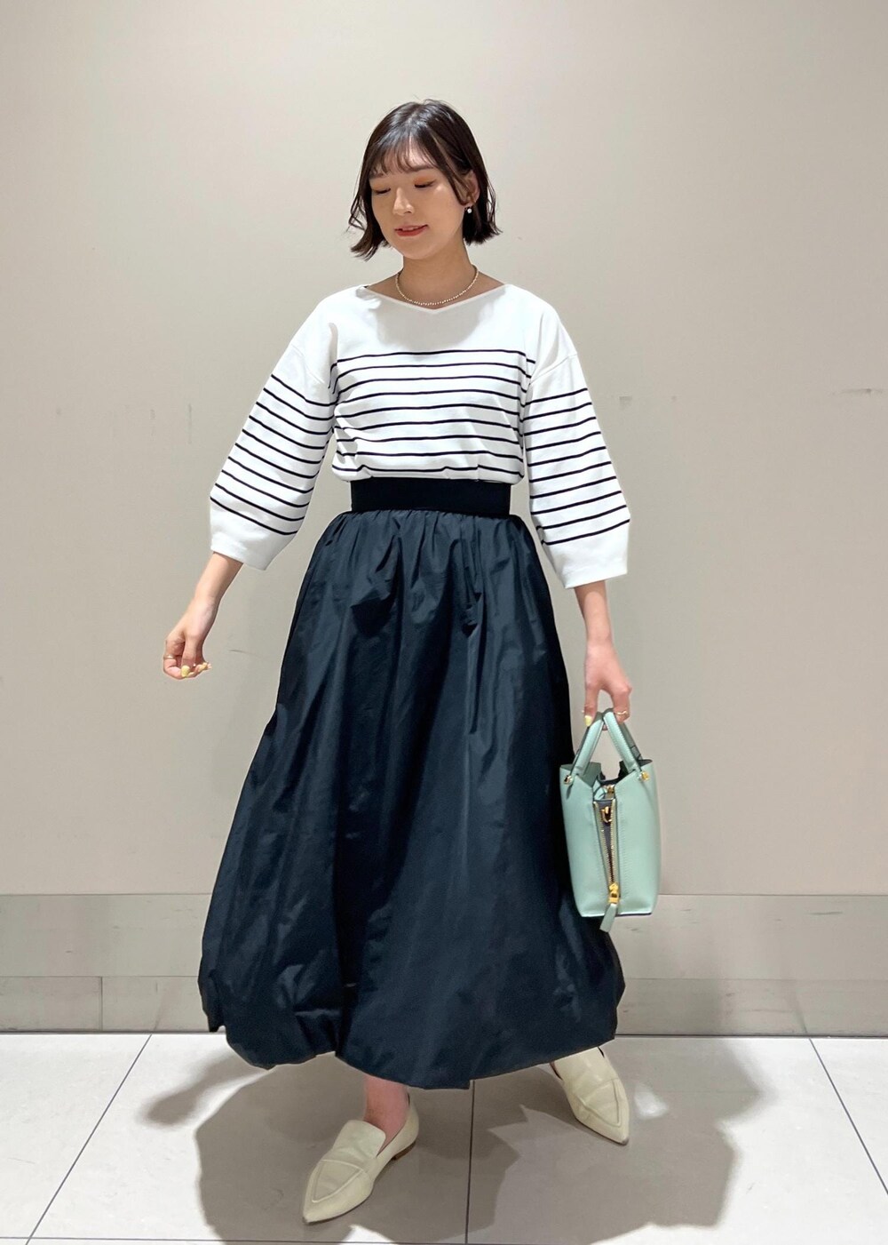 グリーン系のハンドバッグ、ホワイト系のパンプス、ブラック系のスカートを着用したレディースの春コーディネートの3枚目の写真