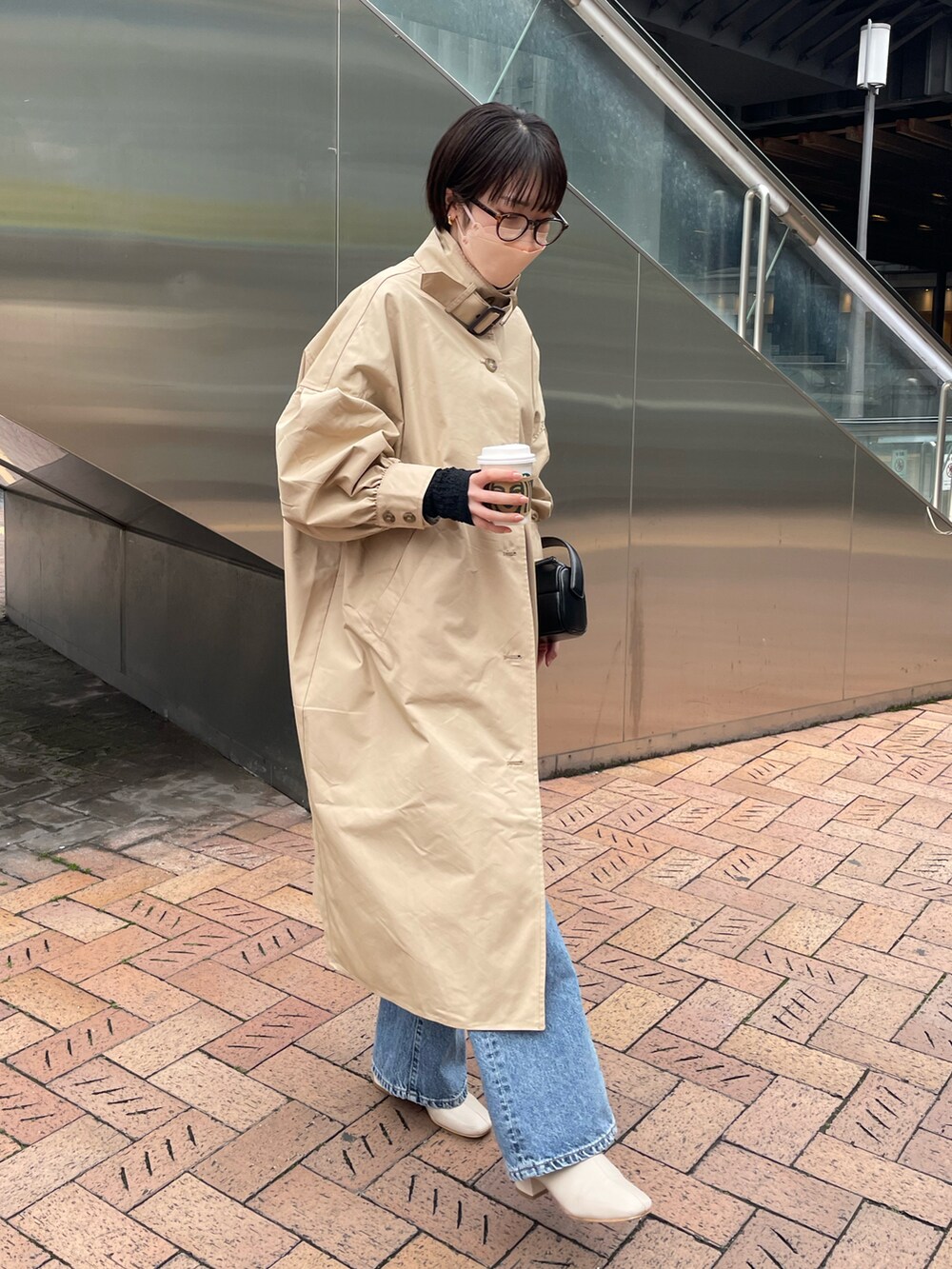 ベージュ系のトレンチコート、ブルー系のデニムパンツ、ブラック系のトートバッグを着用したレディースの冬コーディネートの2枚目の写真