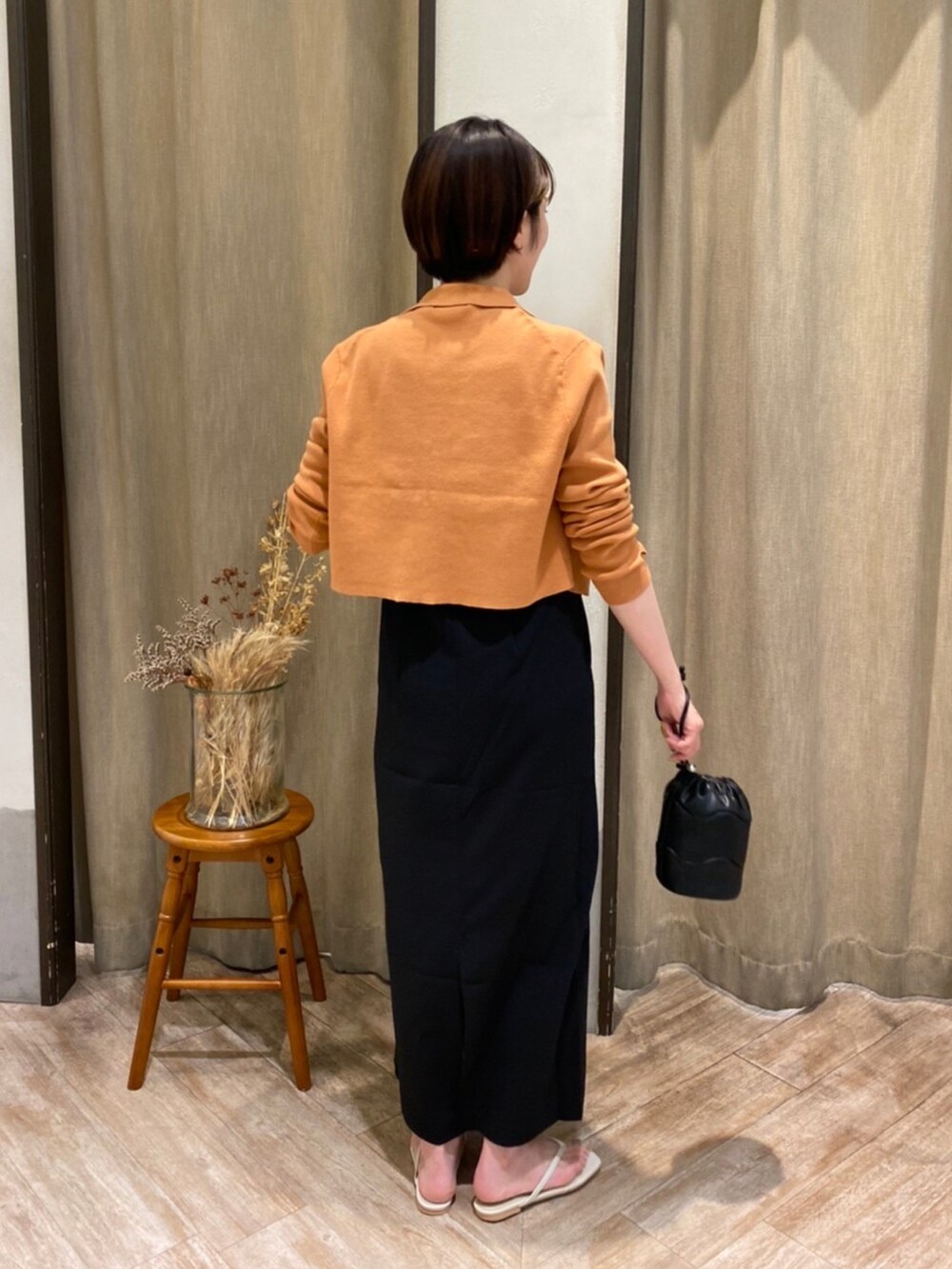 オレンジ系のカーディガン/ボレロ、ブラック系のワンピースを着用したレディースの夏コーディネートの2枚目の写真