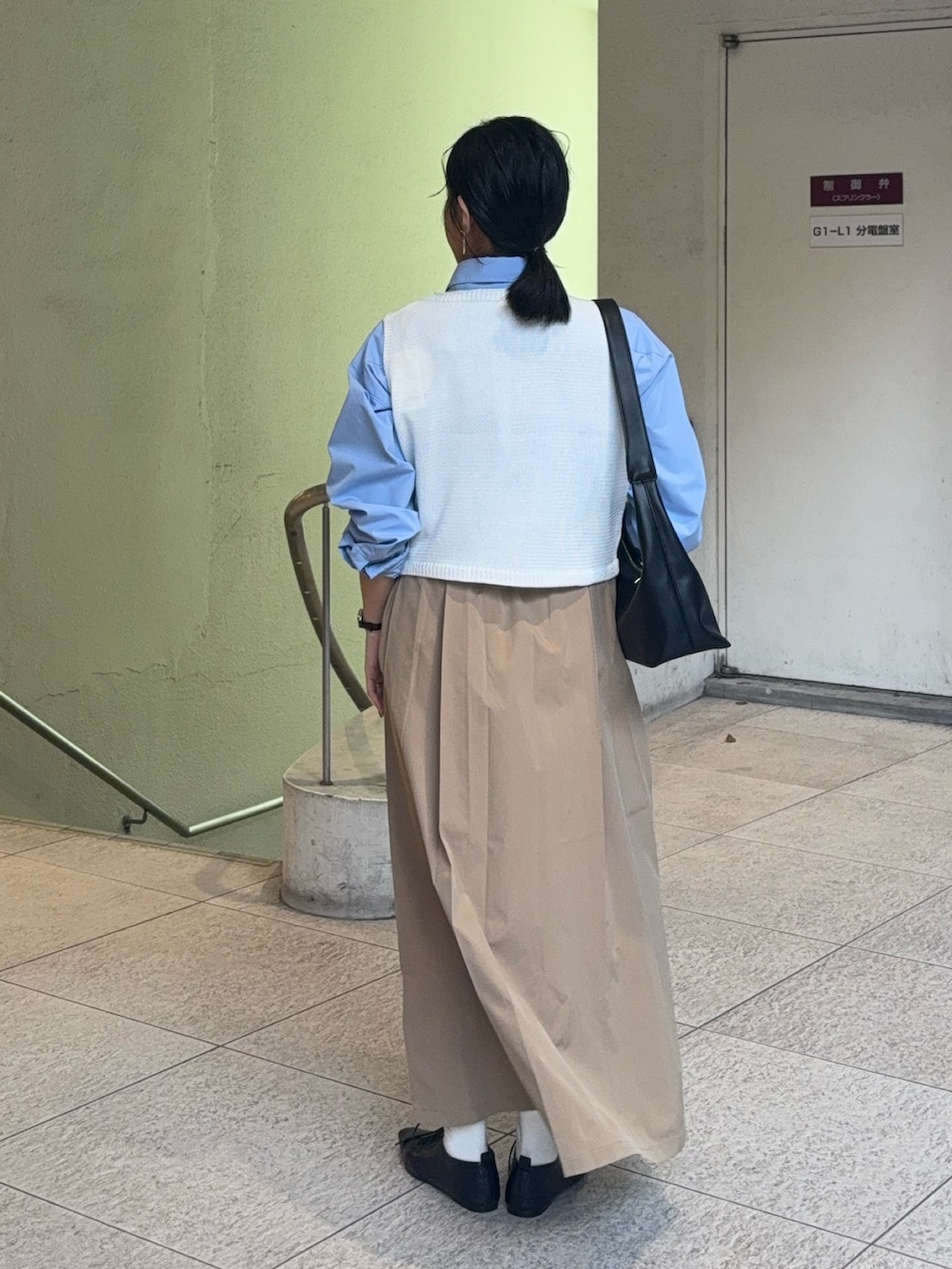 ベージュ系のスカート、ホワイト系のニット/セーター、ブルー系のシャツ/ブラウスを着用したレディースの春コーディネートの2枚目の写真