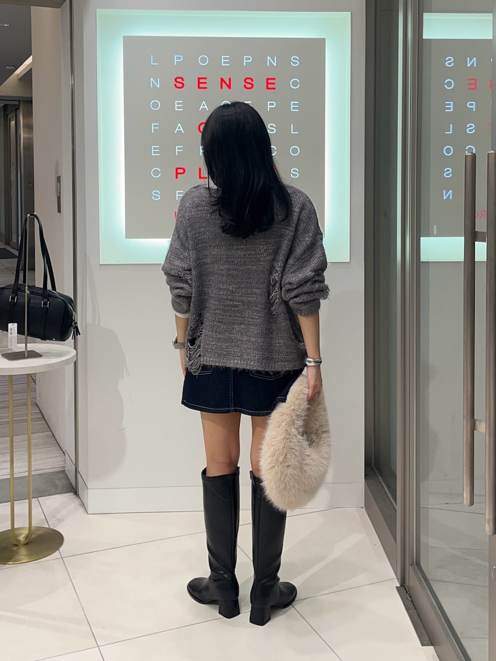 グレー系のニット/セーター、ブルー系のスカート、ホワイト系のTシャツ/カットソーを着用したレディースの秋コーディネートの3枚目の写真