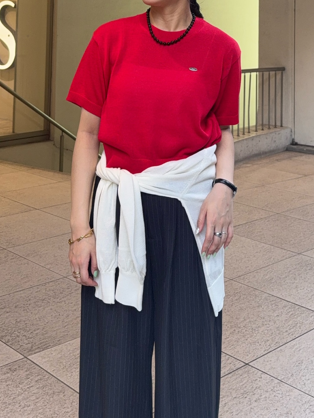 レッド系のニット/セーター、ホワイト系のカーディガン/ボレロ、グレー系のスラックスを着用したレディースの夏コーディネートの4枚目の写真