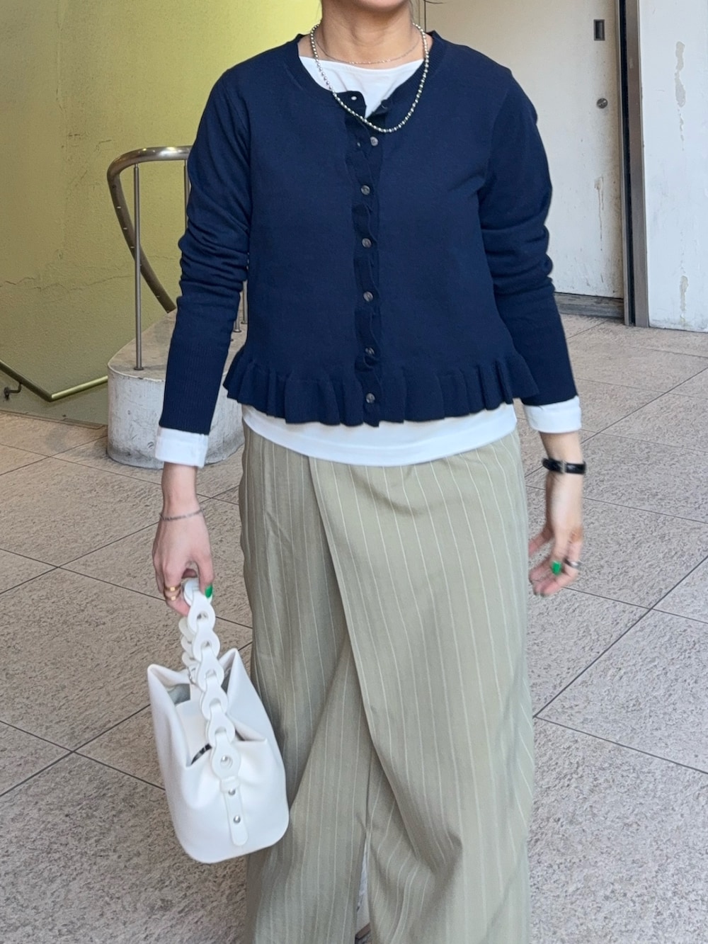 ブルー系のニット/セーター、ベージュ系のスカート、ホワイト系のTシャツ/カットソーを着用したレディースの春コーディネートの2枚目の写真