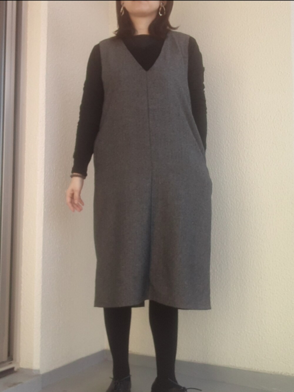 ブラック系のパンプス、グレー系のジャンパースカート、ブラック系のダウンジャケット/コートを着用したレディースの春コーディネートの2枚目の写真