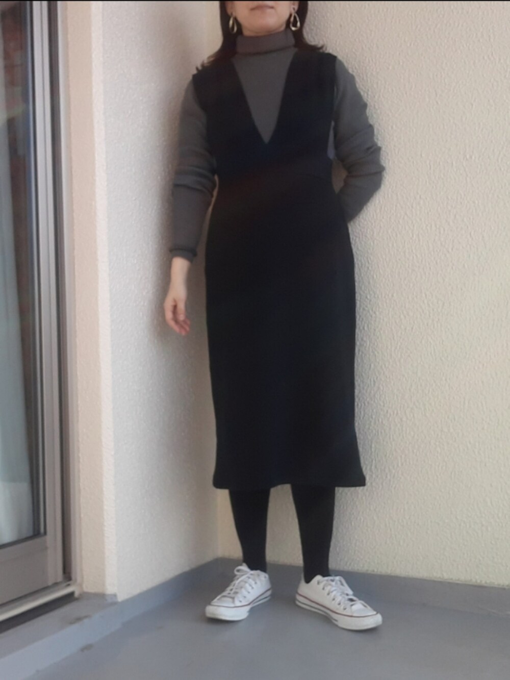 グレー系のニット/セーター、ブラック系のジャンパースカート、ホワイト系のスニーカーを着用したレディースの春コーディネートの2枚目の写真