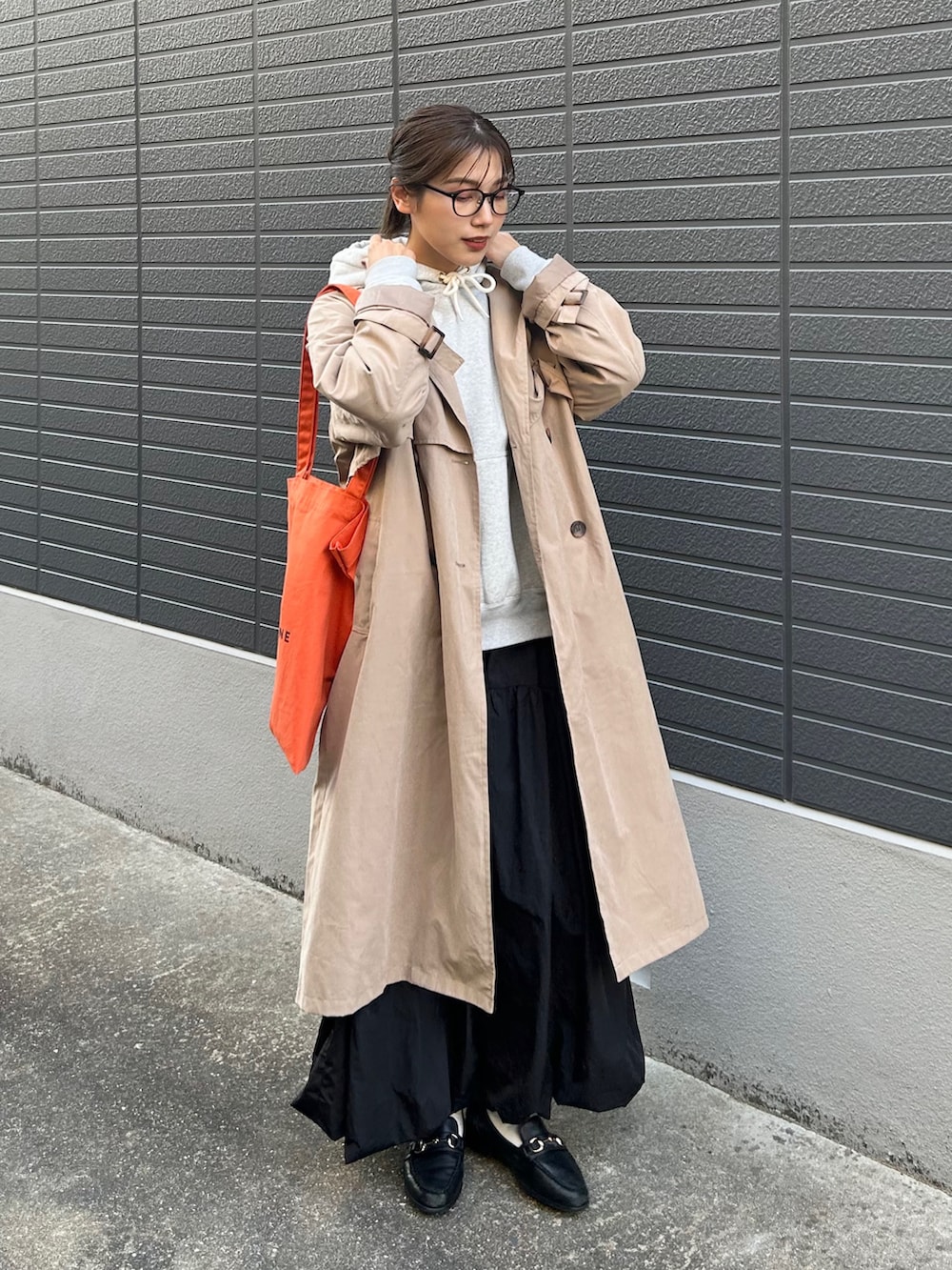 ベージュ系のトレンチコート、グレー系のパーカー、ブラック系のスカートを着用したレディースの春コーディネートの2枚目の写真