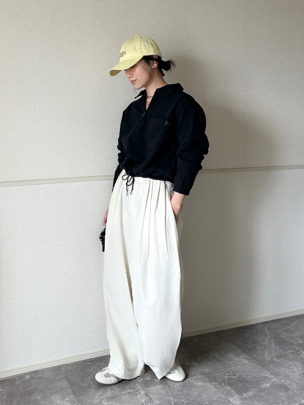 ホワイト系のスラックス、ブラック系のポーチ、ゴールド系のネックレスを着用したレディースの春コーディネートの2枚目の写真