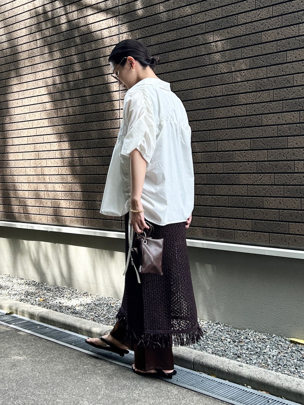 ブラック系のサンダル、ホワイト系のシャツ/ブラウス、ブラウン系のショルダーバッグを着用したレディースの夏コーディネートの2枚目の写真