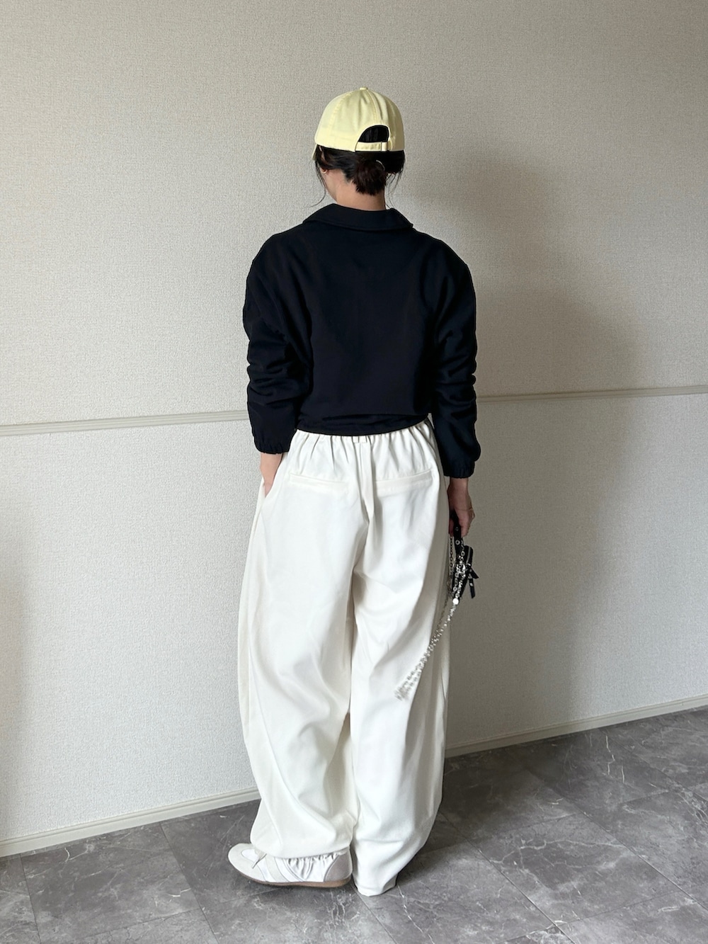 ホワイト系のスラックス、ブラック系のポーチ、ゴールド系のネックレスを着用したレディースの春コーディネートの3枚目の写真