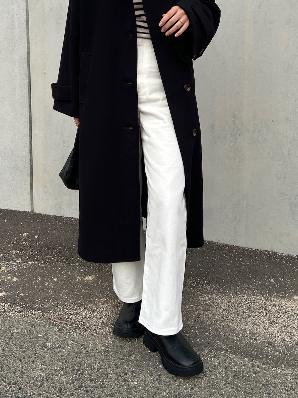 ブラック系のステンカラーコート、ホワイト系のデニムパンツ、ブラック系のブーツを着用したレディースの冬コーディネートの3枚目の写真