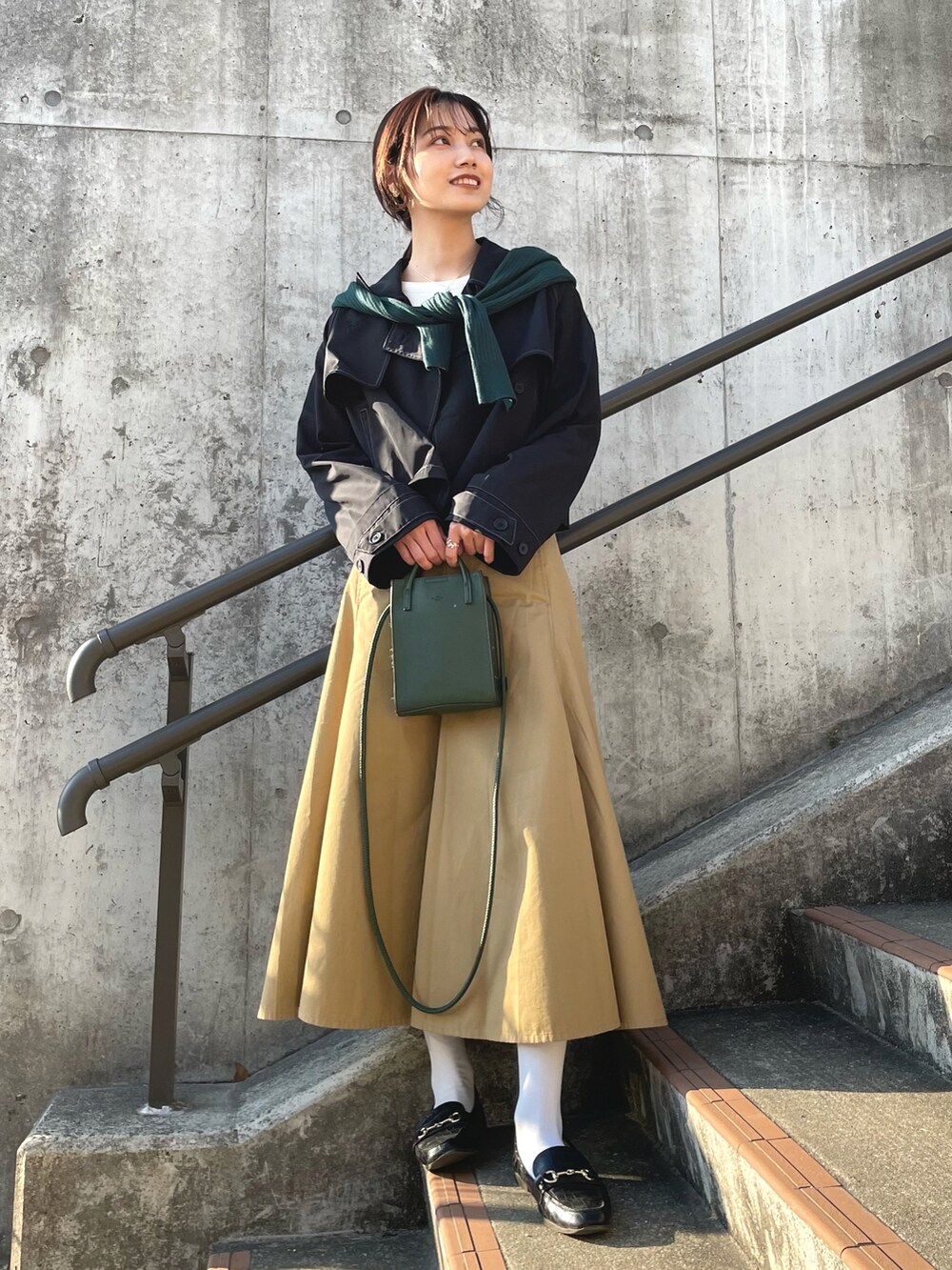 ブラック系のローファー、ブラック系のトレンチコート、グリーン系のショルダーバッグを着用したレディースの春コーディネートの2枚目の写真